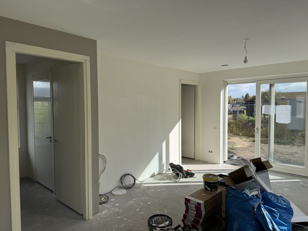 Nieuwbouwwoning tijdens de afbouw met gladde lichte wanden en verfemmers op de betonvloer