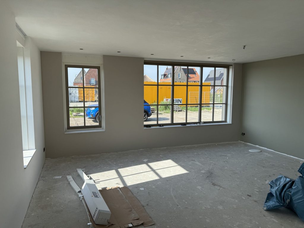 Lege nieuwbouwkamer met grote ramen en wanden die klaar zijn om te worden afgewerkt