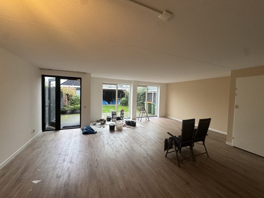 Lege woonkamer met strak gesausde wanden, verfemmers en een trapje bij de tuindeuren