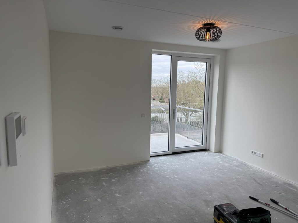 Wit afgewerkte kamer in een nieuw appartement met balkondeur en uitzicht op bomen